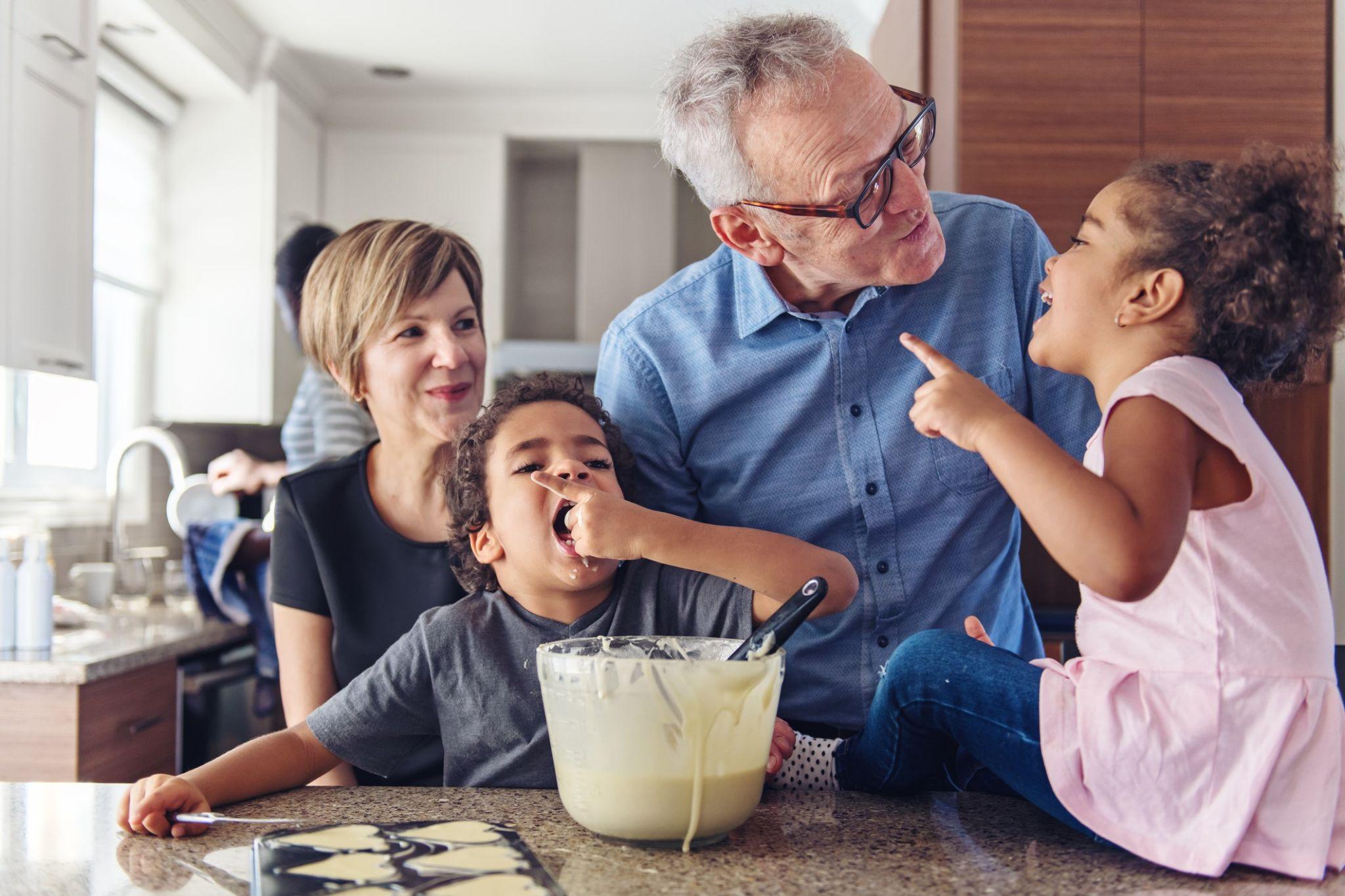 Grandparents laughing and baking with grandchildren in a warm kitchen