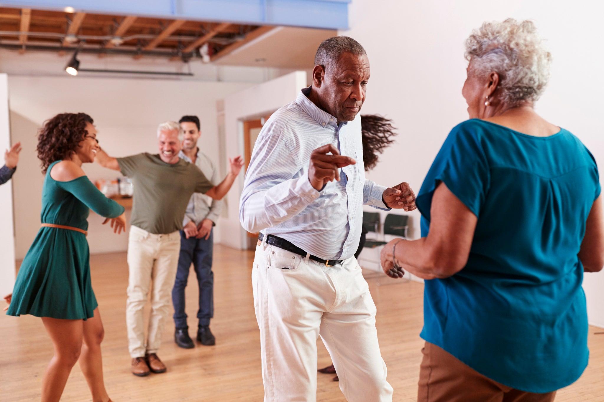 Elderly Black couple dancing energetically with others in a bright, joyful room